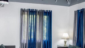 A modern living room with wicker furniture, a glass coffee table, and blue curtains. - High Life Villa (Negril)