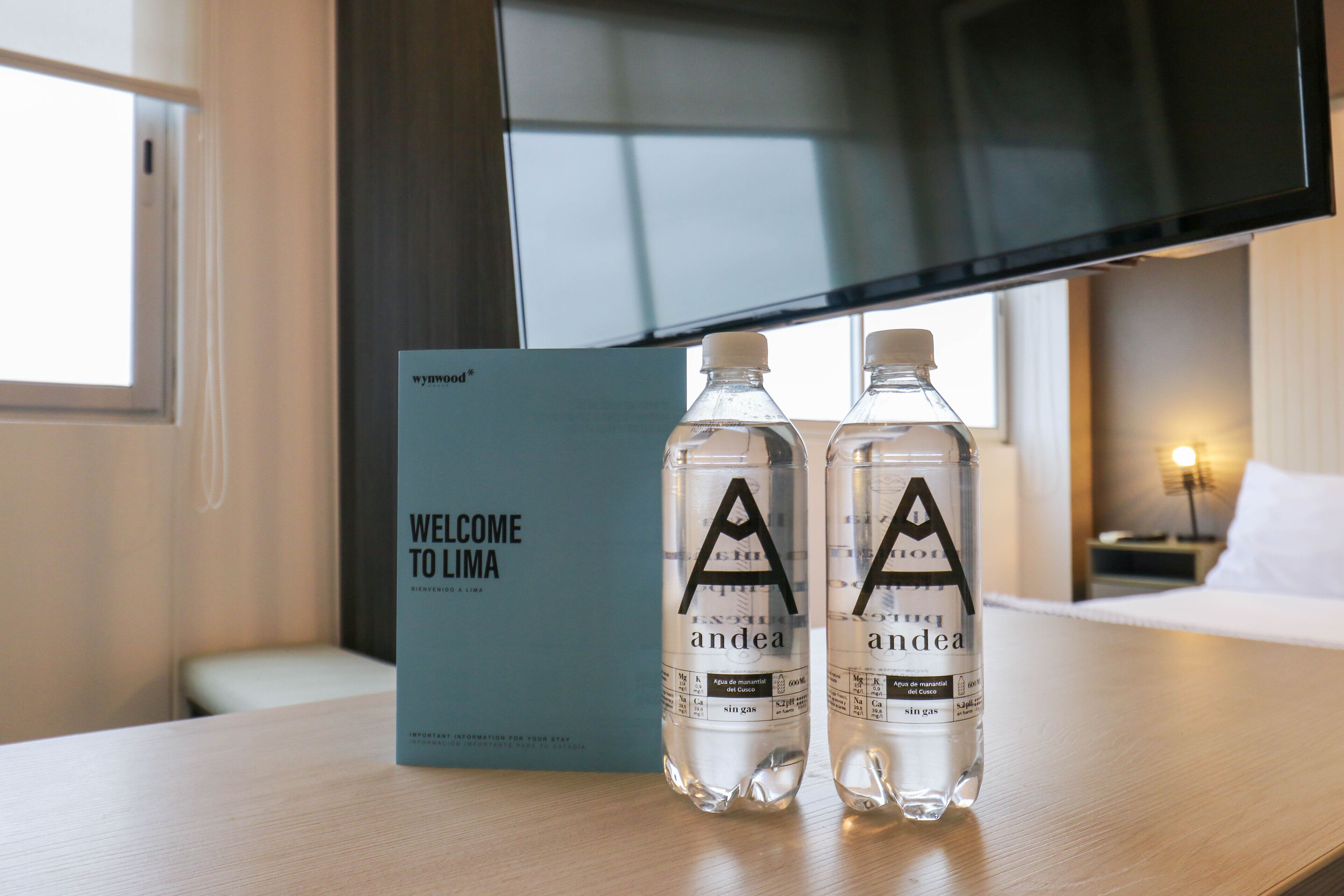 Two bottles of water and a welcome sign on a wooden table in a hotel room.