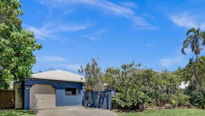 A single-story house with a garage, surrounded by lush greenery and palm trees. - Tranquil Palm Cove Retreat with Heated Pool, Lush Gardens & Steps to the Beach (Palm Cove)