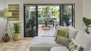 A living room with a sofa, a lamp, and a view of an outdoor patio with a couch and plants. - Tranquil Palm Cove Retreat with Heated Pool, Lush Gardens & Steps to the Beach (Palm Cove)