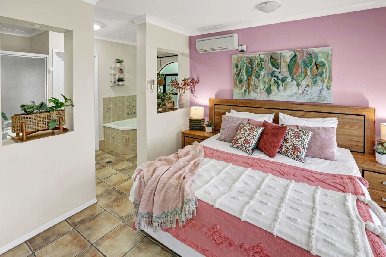 A bedroom with a large bed, a wooden headboard, a pink wall, and a mirror.