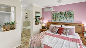 A bedroom with a large bed, a wooden headboard, a pink wall, and a mirror. - Tranquil Palm Cove Retreat with Heated Pool, Lush Gardens & Steps to the Beach (Palm Cove)