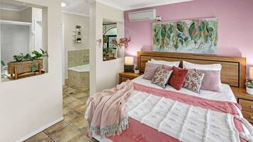 A bedroom with a large bed, a wooden headboard, a pink wall, and a mirror.