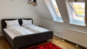 Ett sovrum med en säng, en röd matta, ett takfönster och ett element.