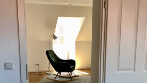 Ett rum med trägolv, en gungstol, en lampa och en vit dörr.