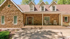 A stone house with a stone facade, a front porch with two rocking chairs, and a small porch area with a bench and a cart. - Wooded Luxury Home (Ashtabula)