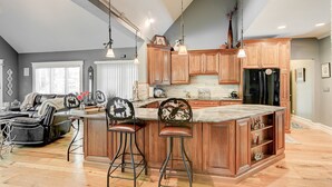 A spacious kitchen with wooden cabinets, a large island with bar stools, and pendant lighting. - Wooded Luxury Home (Ashtabula)
