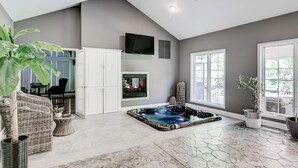 A spacious room with a large window, a hot tub, and a television on the wall. - Wooded Luxury Home (Ashtabula)