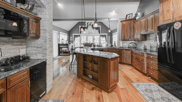 A spacious kitchen with wooden cabinets, a central island, and a stone accent wall. - Wooded Luxury Home (Ashtabula)