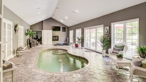 A spacious indoor pool area with a curved design, surrounded by stone flooring and large windows. - Wooded Luxury Home (Ashtabula)