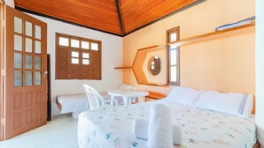 Quarto com cama, uma mesinha e uma cadeira. Tem uma porta e janelas com persianas.