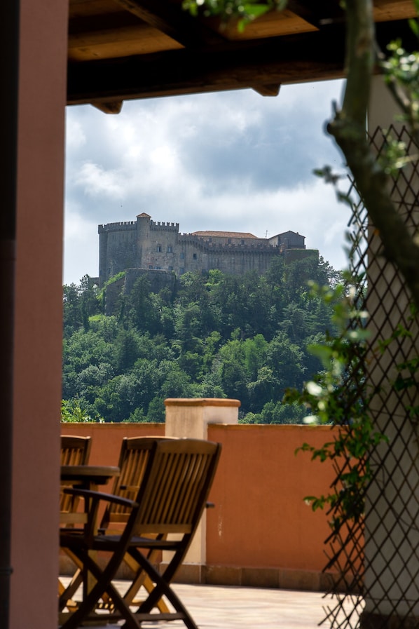 Vue d’un château perché sur une colline, prise depuis un balcon doté de chaises en bois et d’un sol carrelé.