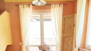 Ein Essbereich mit Holztisch und weißen Stühlen, einer Blumenvase und Blick durch ein mit Vorhängen drapiertes Fenster.