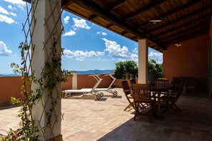 Une terrasse extérieure avec une table et des chaises, une chaise pliante blanche et un chariot.