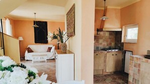 Una sala de estar acogedora con sofá, una mesa de comedor con sillas y una zona de cocina con armarios y salpicadero de azulejos.