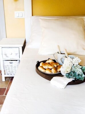 Un lit bien fait, avec un plateau de viennoiseries, une tasse et un bouquet de fleurs sur la table de chevet.