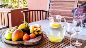 Una mesa de madera con un frutero, una jarrón de agua con rodajas de limón y dos copas de vino.