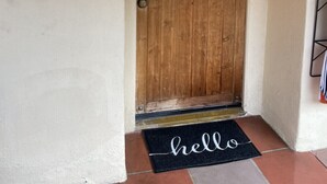 Una porta de fusta amb una placa on hi figura el número '3', un felpú negre amb la paraula 'hello' escrita i una làmpada fixada a la paret.