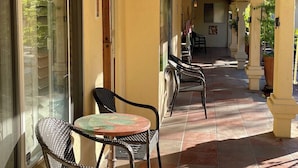 Zona exterior coberta amb cadires de vimet i taula, una porta de vidre i un paviment de rajoles.