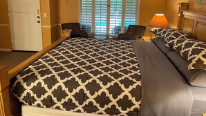Una habitació d'hotel amb un llit gran, una taula amb cadira, un frigorífic i una finestra amb persianes.