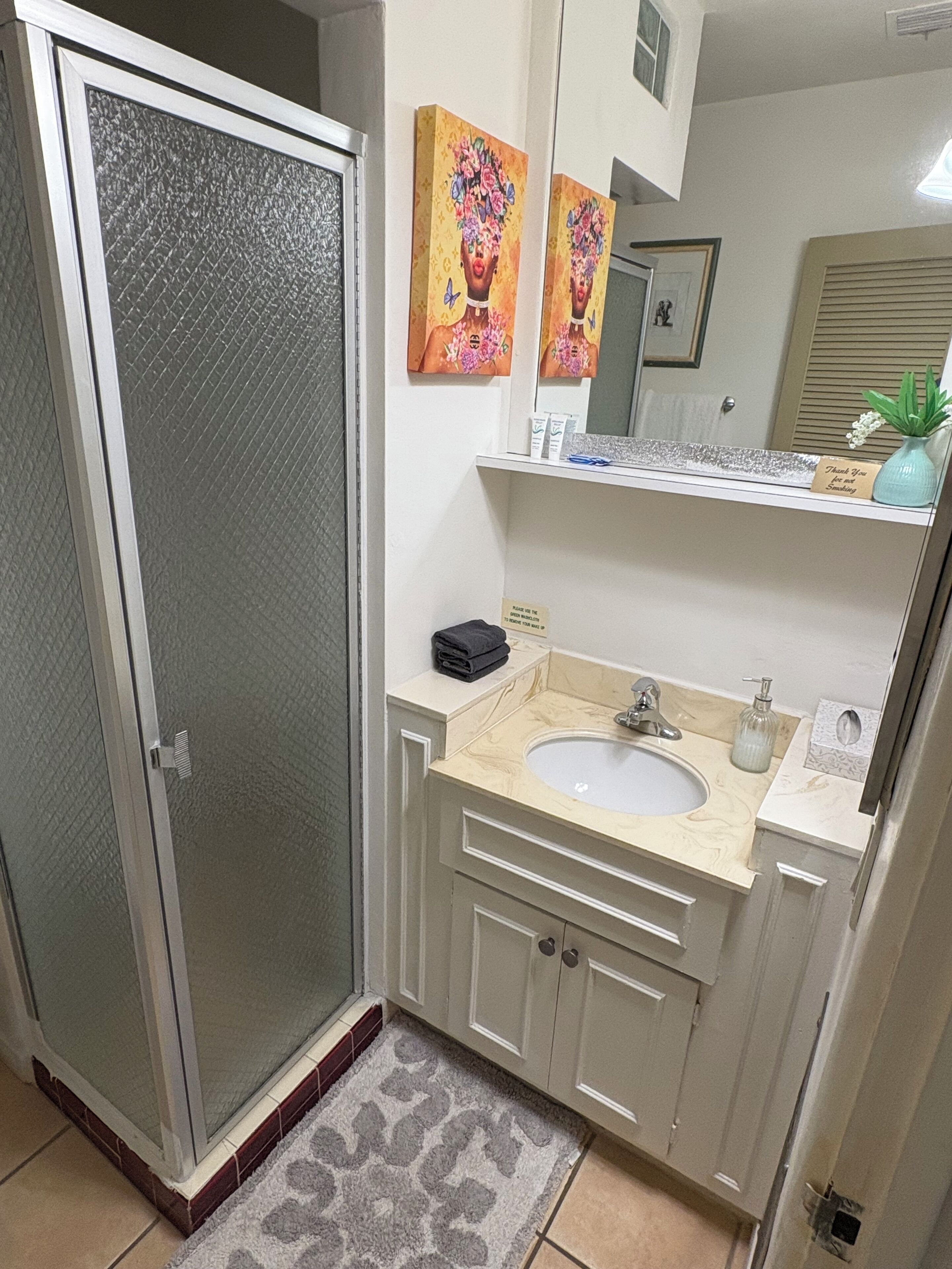 A bathroom with a shower, a sink, and a mirror. There are towels and toiletries on the counter.