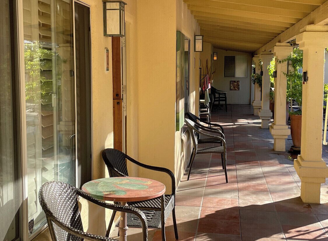 Un espace extérieur abrité, doté de chaises et d’une table en osier, d’une porte vitrée et d’un sol carrelé.