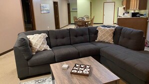 Ein Wohnzimmer mit Ecksofa, Couchtisch und einem Essbereich im Hintergrund.