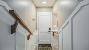 A narrow hallway with a white door at the end, wooden handrails, and a small rug at the entrance. - 2BR Stylish Suite: Outlets & REC Room|Sep Entrance (Edmonton)