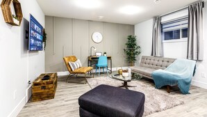 A modern living room with a sofa, ottoman, coffee table, and a desk with a chair. - 2BR Stylish Suite: Outlets & REC Room|Sep Entrance (Edmonton)