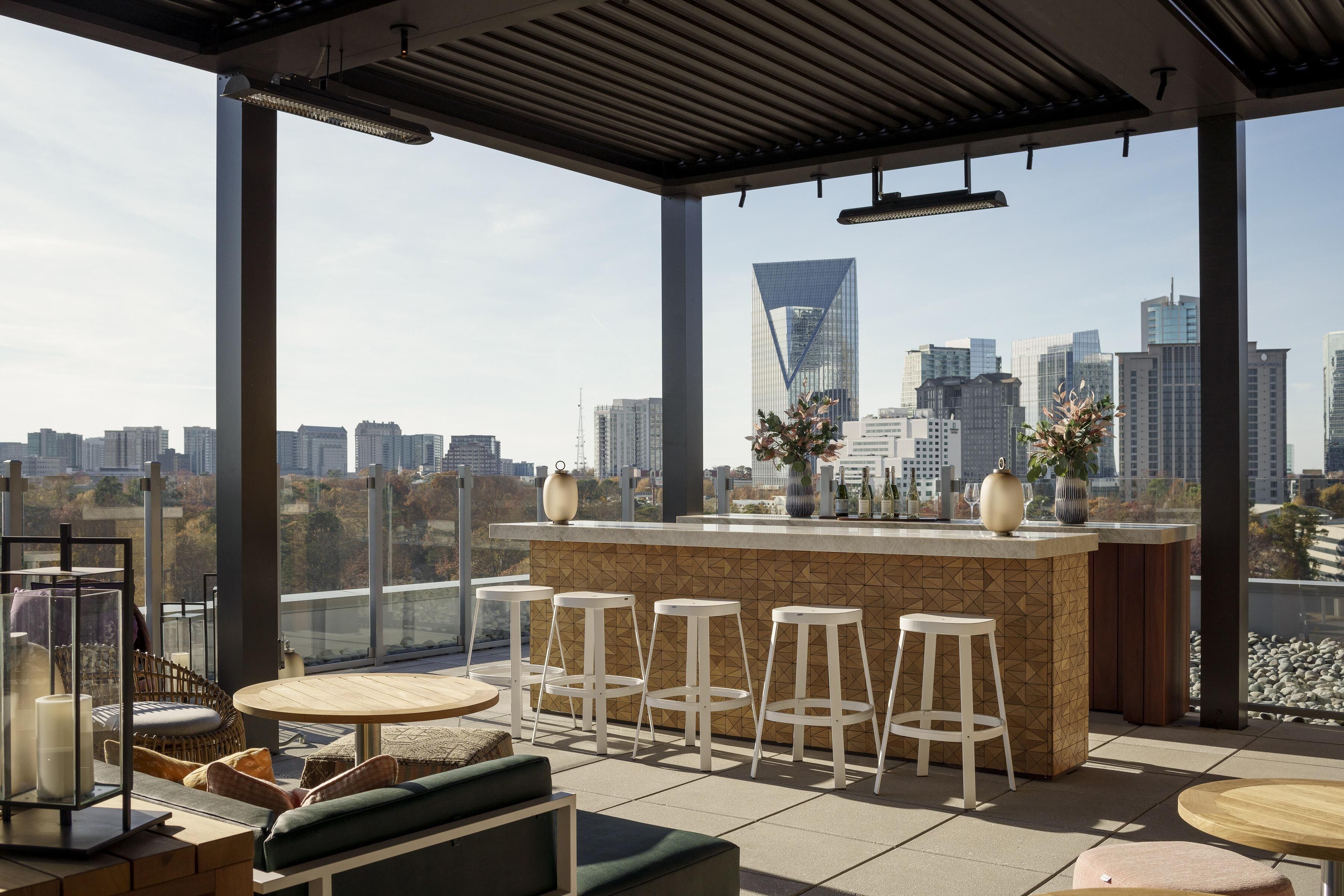A rooftop bar with a city view, bar stools, and seating areas.