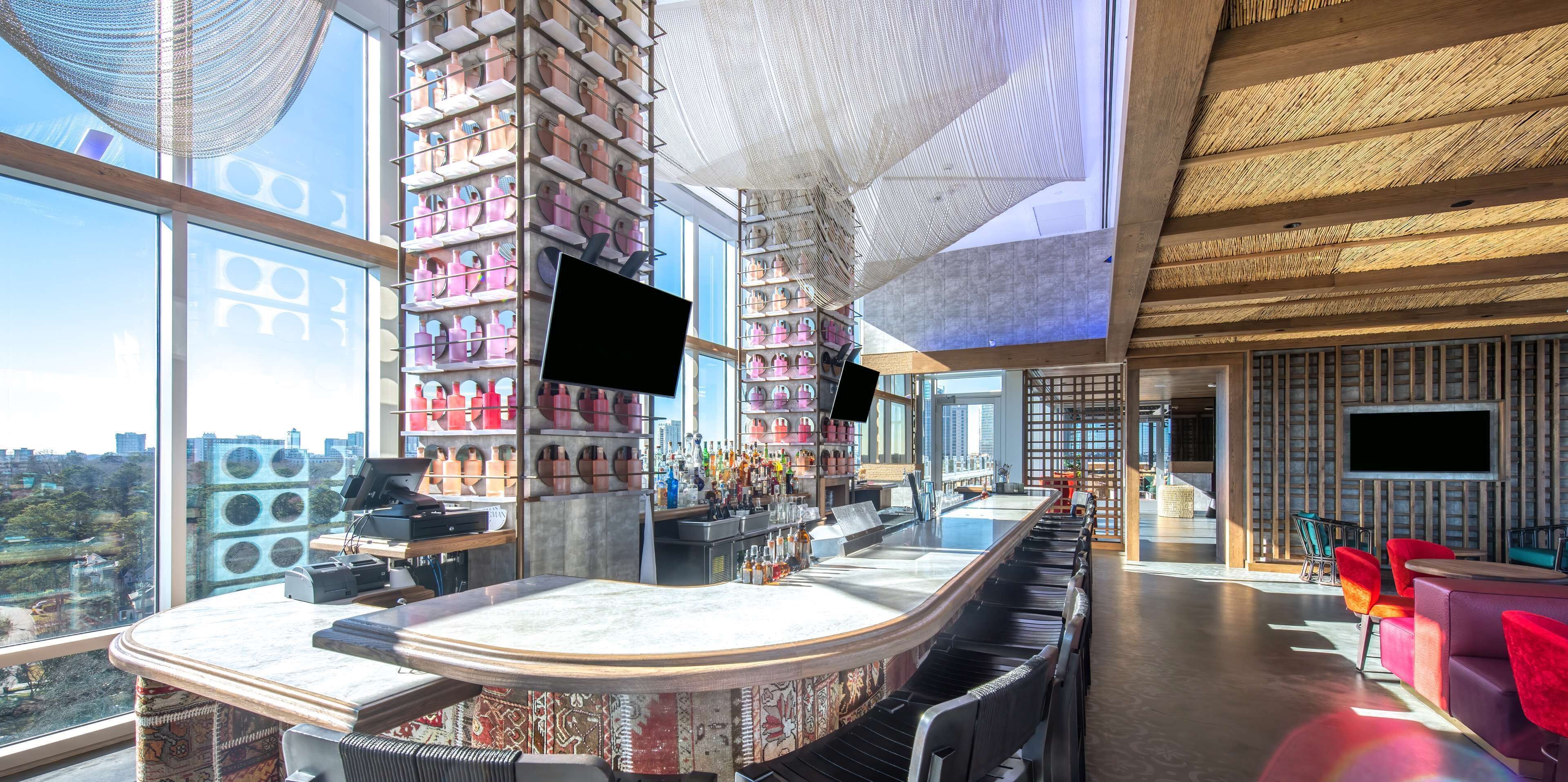 A modern bar area with a long counter, shelves with bottles, and a large TV screen.
