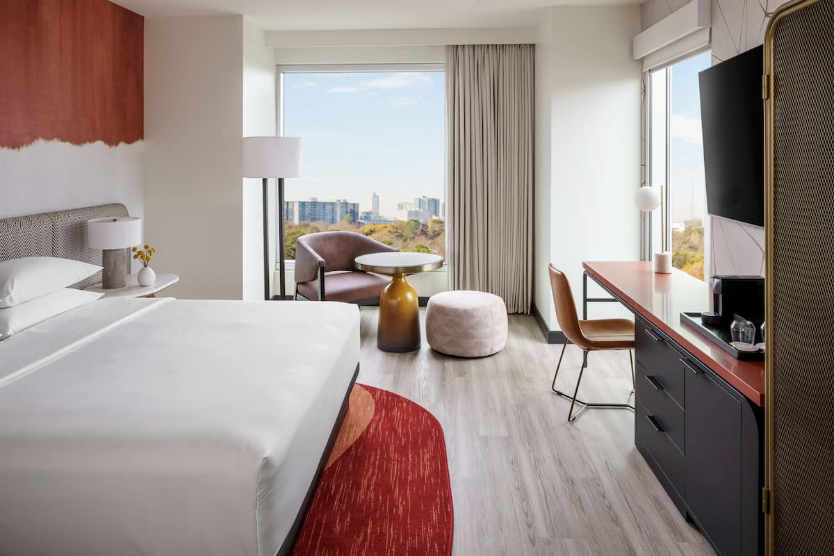 A hotel room with a large bed, a desk, a chair, a round table, and a TV.