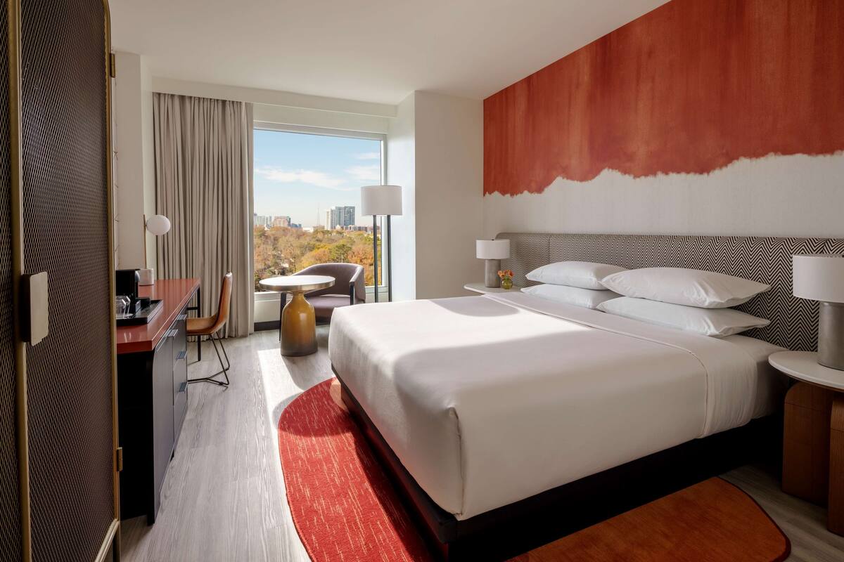 A hotel room with a large bed, a desk, a chair, and a view of the city.