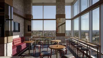 A modern interior with a red sofa, round tables, and bar stools, large windows offering a city view.