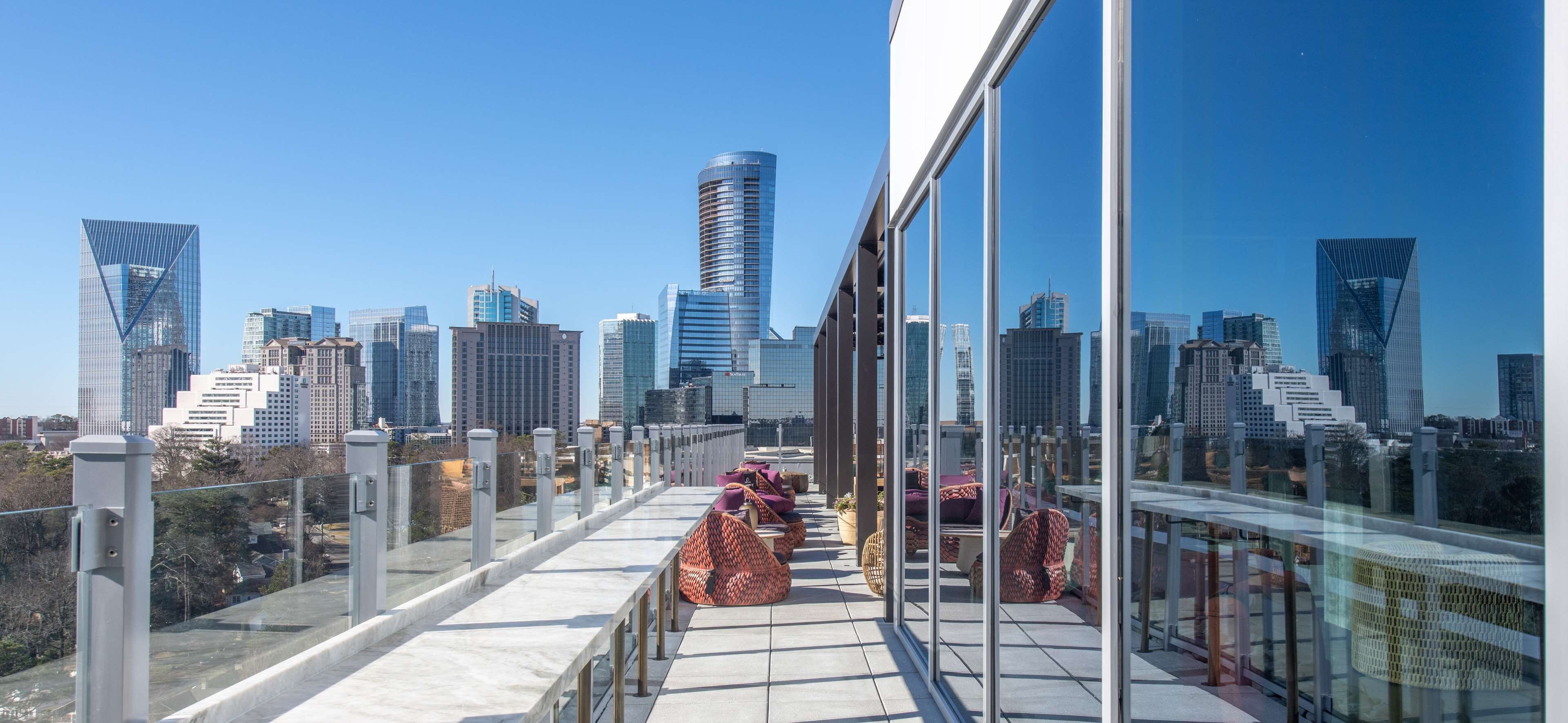 A rooftop terrace with a city skyline view, featuring modern buildings and a glass railing.