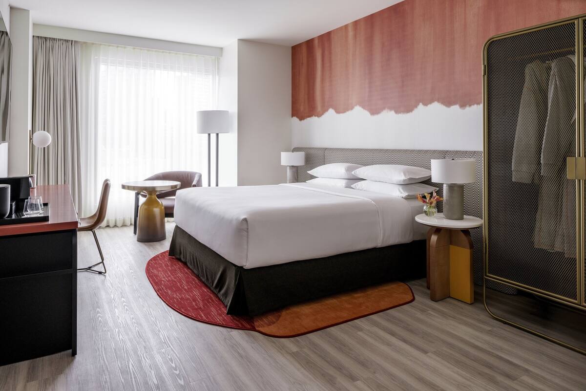 A hotel room with a large bed, a desk, a chair, a round table, a lamp, and a wardrobe.