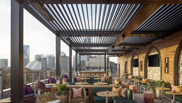 Eine Dachterrasse mit Sitzbereichen, einer Bar und Blick auf die Stadt.