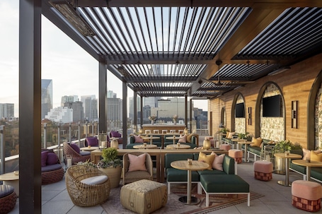 A rooftop lounge with seating areas, a bar, and a city view.