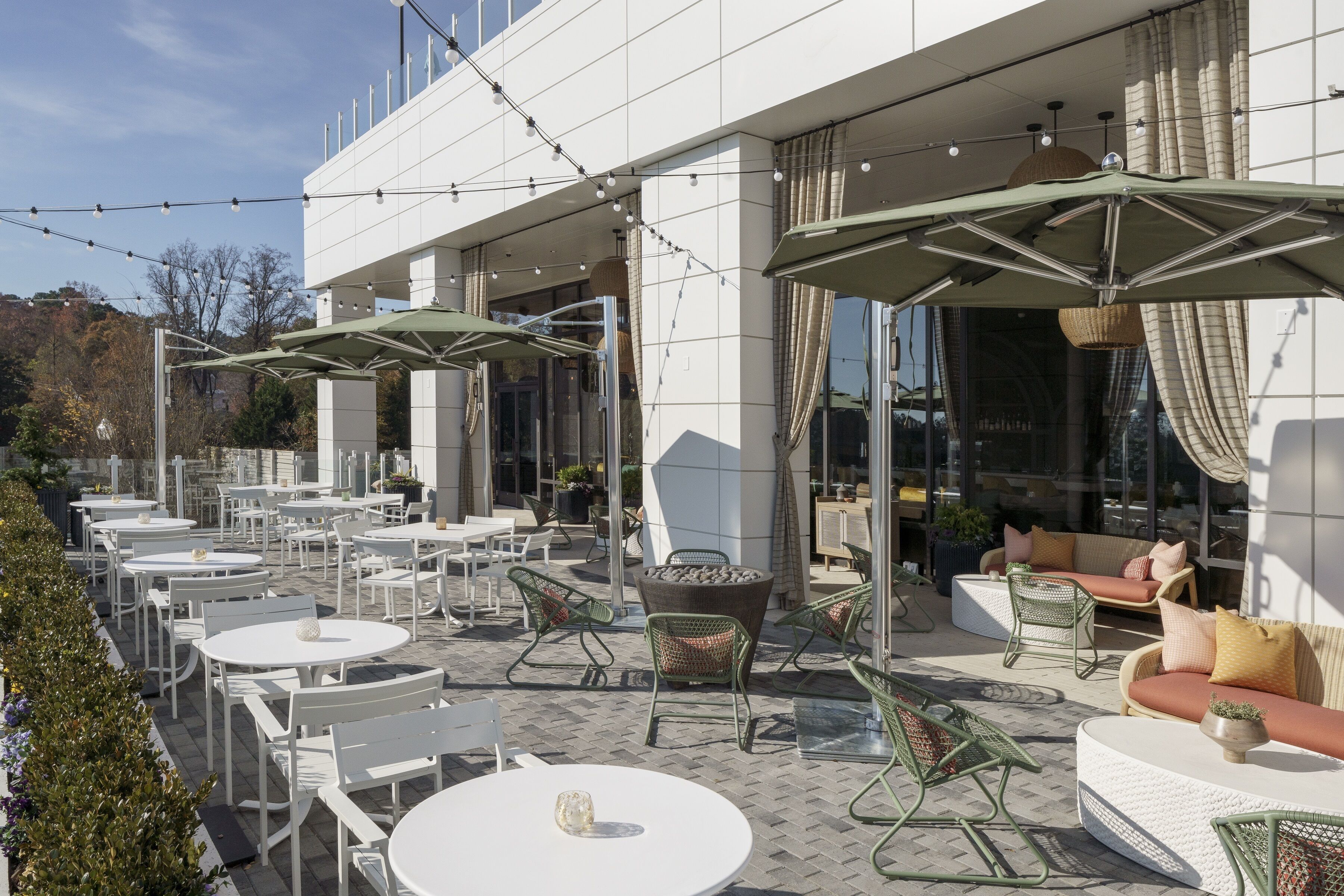 An outdoor patio with round tables and chairs, umbrellas, and wicker furniture.