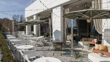 An outdoor patio with round tables and chairs, umbrellas, and wicker furniture.