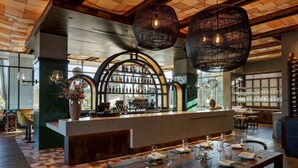 Ein Restaurant mit Barbereich, Holztischen und hängenden Korbtreleuchtern.