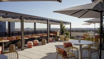 An outdoor seating area with tables and chairs, a covered section with a view of the cityscape.