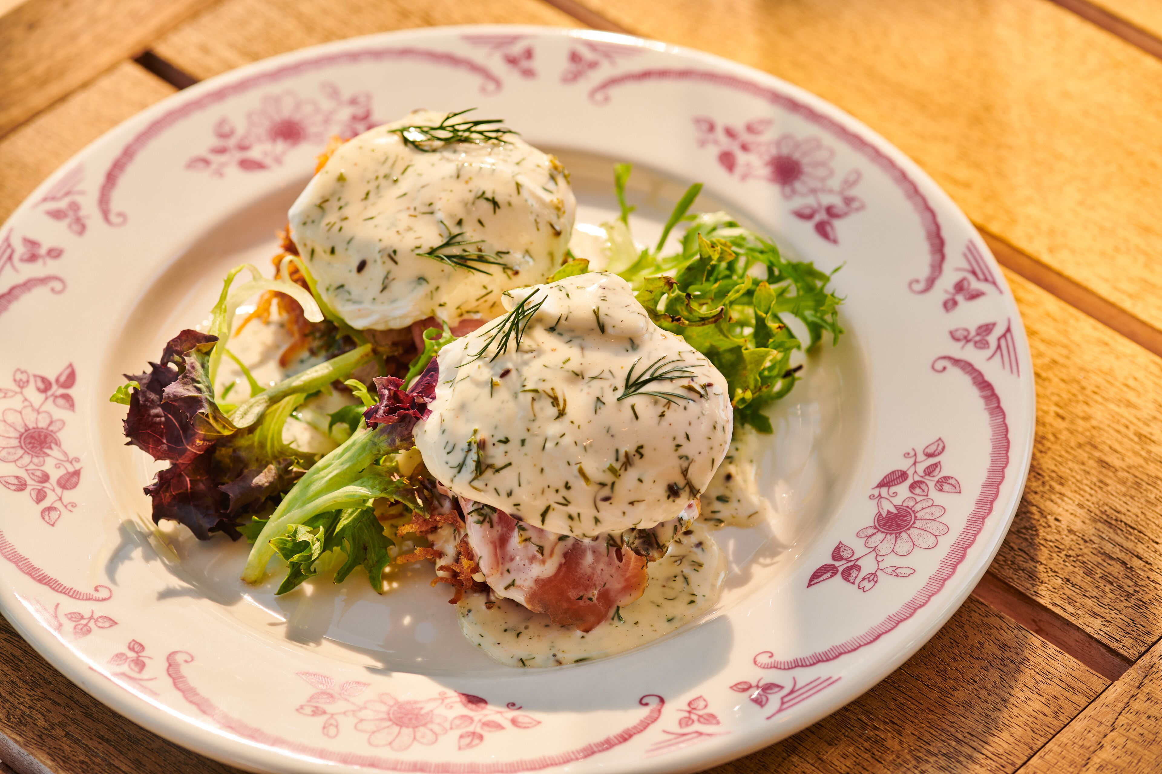 A plate of food with a floral pattern on the rim, containing a salad and two poached eggs with a creamy sauce.