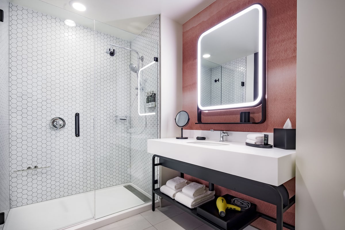 A modern bathroom with a glass shower enclosure, a white sink with a mirror, and a black vanity.
