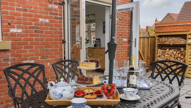 Une table ronde en métal, sur laquelle se trouve un plateau avec de la nourriture et des boissons, entourée de chaises, le tout placé devant un mur de briques.