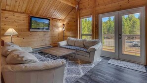 A cozy cabin interior with a wooden ceiling, a sofa, a coffee table, and a TV mounted on the wall. - Mountain Memories in Homewood (Tahoma)