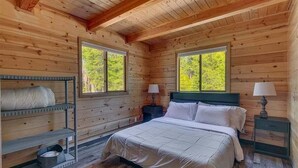 A wooden cabin bedroom with a bed, two nightstands, a shelf with a mattress, and two windows. - Mountain Memories in Homewood (Tahoma)