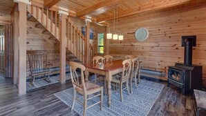 A wooden interior with a dining table, chairs, a staircase, and a wood-burning stove. - Mountain Memories in Homewood (Tahoma)