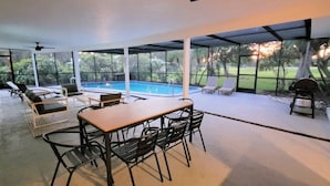 Uma área externa coberta com piscina, espreguiçadeiras e uma mesa com cadeiras.