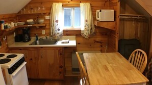 A compact kitchen with wooden cabinets, a stove, a microwave, and a dining table with chairs. - Studio Suite 1 with full kitchen  (Stratton)